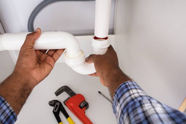 Plumbers hands fixing piping below a sink